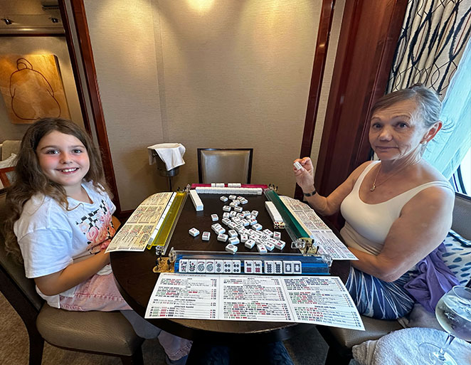 Family playing mahjong at a round table with tiles and scorecards for the Mahjong Baby About Us page Family playing mahjong at a round table with tiles and scorecards for the Mahjong Baby About Us page